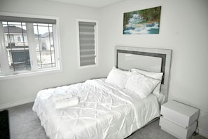 A bedroom with a bed, a window, a painting, and a nightstand.
