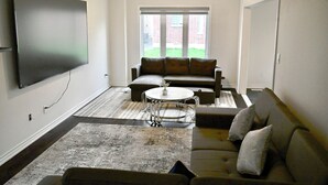 A living room with a flat-screen TV, a sectional sofa, a round coffee table, and a patterned rug. - Elegant 4-Bedroom Luxury Retreat with 2 Sofa Beds, Close to Niagara Falls (Thorold)