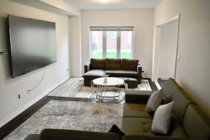 A living room with a flat-screen TV, a sectional sofa, a round coffee table, and a patterned rug.