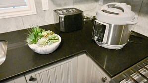 A kitchen with a toaster, a slow cooker, and a bowl of flowers on the counter. - Elegant 4-Bedroom Luxury Retreat with 2 Sofa Beds, Close to Niagara Falls (Thorold)