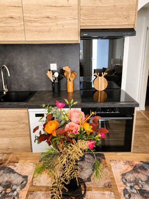 Une cuisine moderne avec des meubles en bois, un plan de travail noir, un lave-vaisselle, un four et un vase de fleurs posé sur le plan de travail.