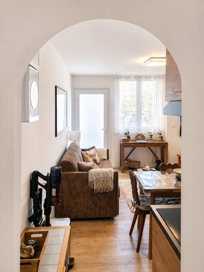 Un espace de vie compact comprenant un canapé, une table à manger, un coin cuisine et une grande fenêtre.