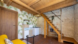 Un plafond en bois, un escalier, un canapé jaune, un meuble blanc et un mur en pierre.