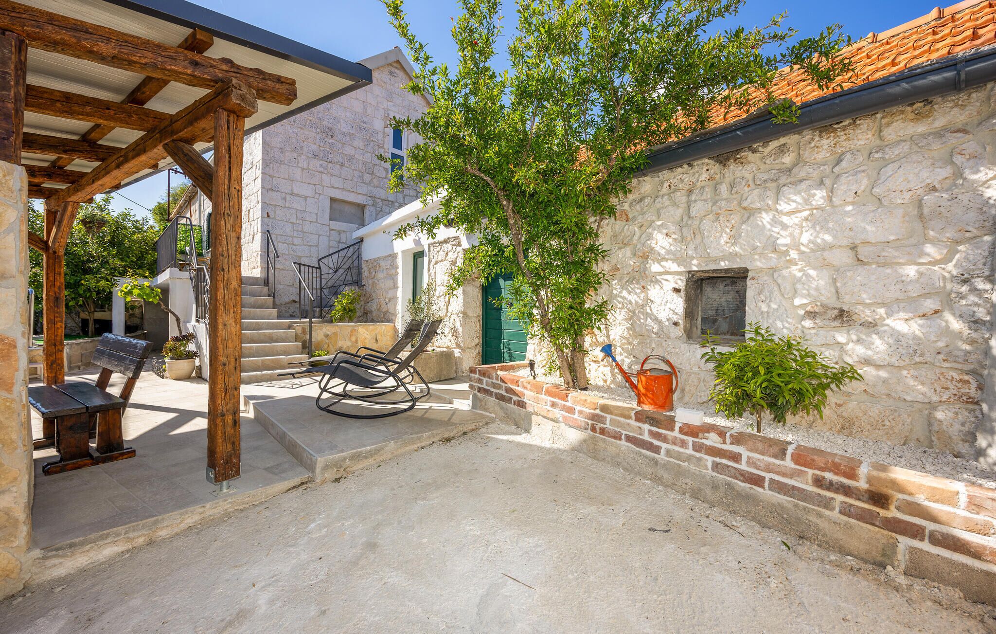 A stone building with a wooden pergola, outdoor seating, and a tree.