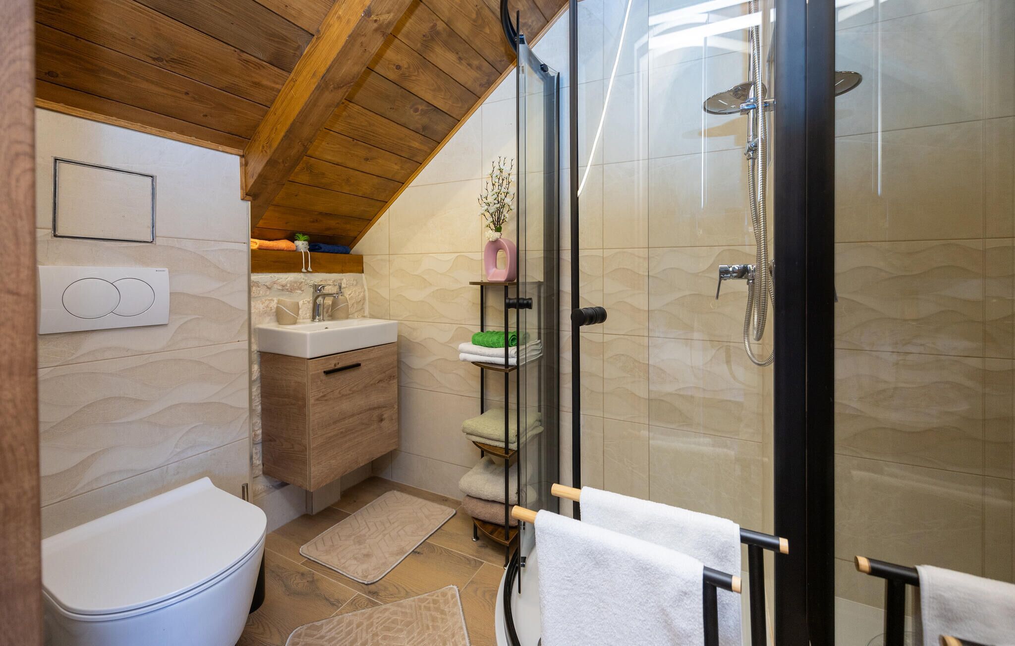 Een badkamer met douche, toilet, wastafel en een houten wastafelmeubel.
