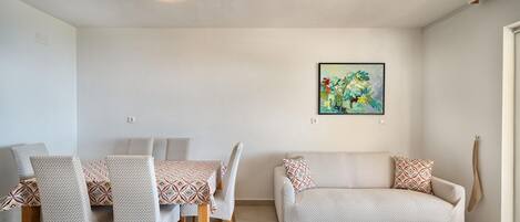 A living room with a sofa, chairs, a dining table, and a painting on the wall.