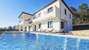 Ein modernes, zweistöckiges Haus mit Swimmingpool, überdachter Terrasse und Blick auf die Umgebung.