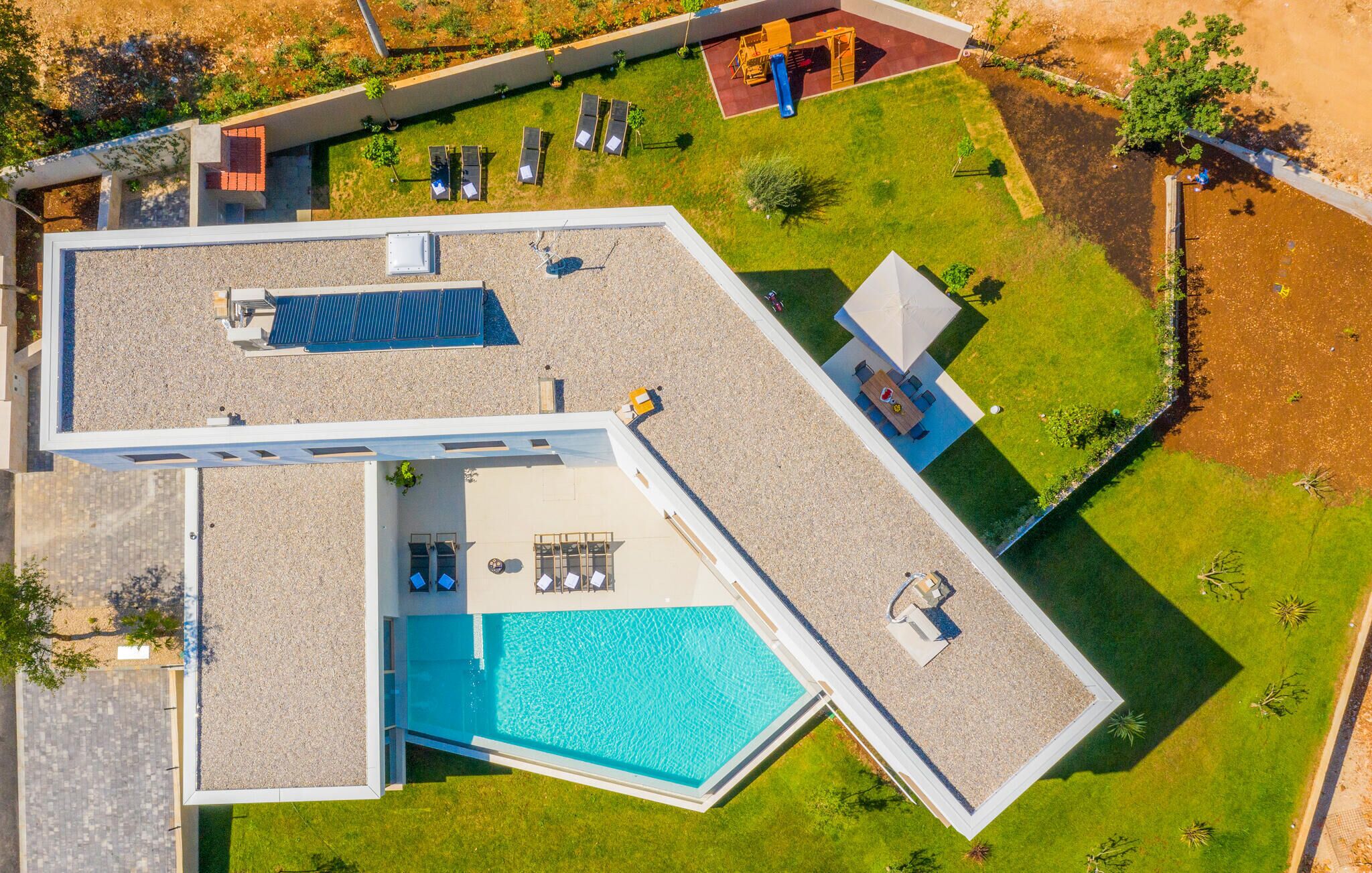 Een modern huis met een zwembad, een terras met zitplaatsen en een kleine tuin.