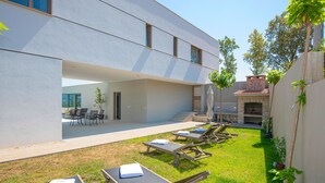 Une terrasse extérieure moderne, dotée de chaises longues, d’un espace barbecue et d’un coin salon avec tables et chaises.