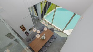Un espace repas moderne avec une table en bois et des chaises grises, une cloison en verre et une vue sur une piscine.