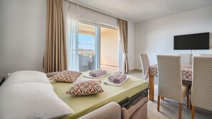 Et hotelværelse med seng, fjernsyn, balkon med gardiner og et spiseområde med stole.