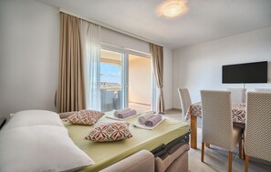 A hotel room with a bed, a TV, a balcony with curtains, and a dining area with chairs. - Cozy apartment in Bast with swimming pool (Bast)