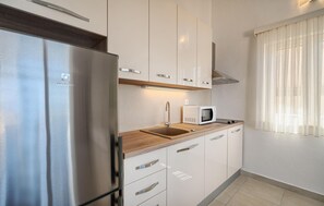 A modern kitchen with stainless steel appliances, white cabinetry, a wooden countertop, and a window with sheer curtains. - Cozy apartment in Bast with swimming pool (Bast)