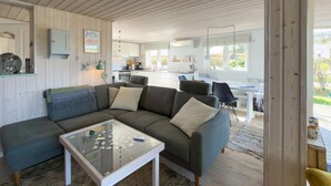 A modern living room with a sectional sofa, a glass coffee table, and a kitchen in the background. - 3 bedroom amazing home in Ebeltoft (Ebeltoft)