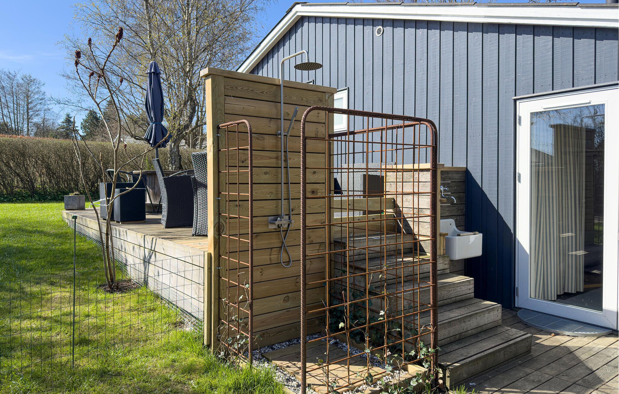 Une terrasse en bois avec un portail en métal, un petit espace extérieur aménagé pour s’asseoir et un bâtiment doté d’une porte-fenêtre coulissante.