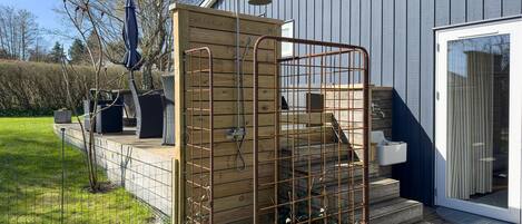 Une terrasse en bois avec un portail en métal, un petit espace extérieur aménagé pour s’asseoir et un bâtiment doté d’une porte-fenêtre coulissante.