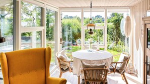 A room with a yellow armchair, a round table with a white tablecloth, wicker chairs, and large windows offering a view of greenery. - 3 bedroom amazing home in Ebeltoft (Ebeltoft)