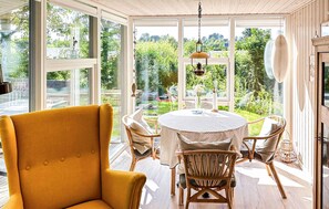 A room with a yellow armchair, a round table with a white tablecloth, wicker chairs, and large windows offering a view of greenery. - 3 bedroom amazing home in Ebeltoft (Ebeltoft)