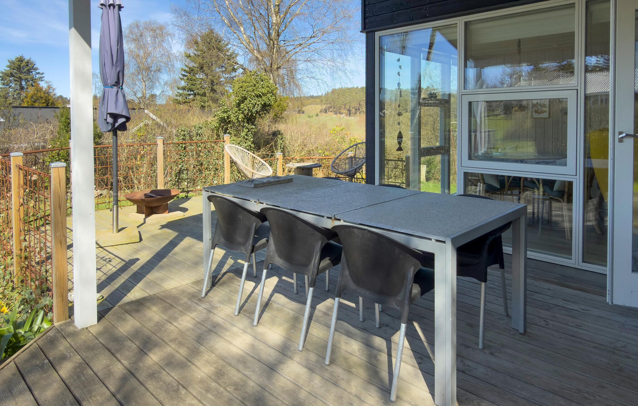 Une terrasse avec une table et des chaises, une porte vitrée et une vue sur l’extérieur.