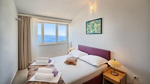 Habitación de hotel con cama, mesita de noche, lámpara, ventana con cortinas y un cuadro en la pared.