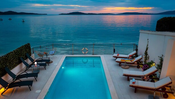Una piscina con sillones de descanso y vistas al mar al atardecer.