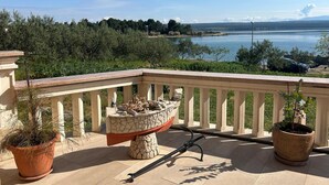 A balcony with a stone planter, potted plants, and a view of a lake and mountains. - Beautiful apartment in Raslina with WiFi (Raslina)
