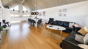 Un vaste espace de vie comprenant une cuisine moderne, une table à manger avec des chaises, un canapé en cuir noir et des œuvres d’art accrochées aux murs.