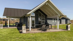 Une maison moderne dotée d’un patio couvert, de grandes fenêtres et d’une pelouse bien entretenue.