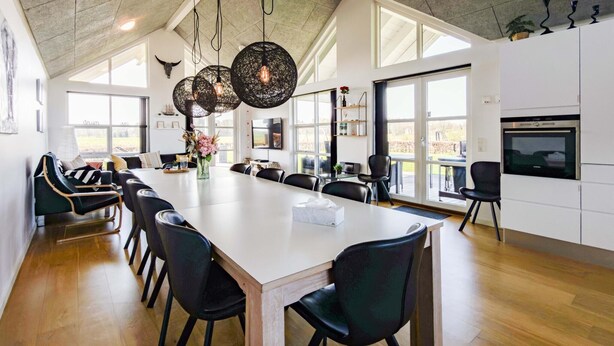Un vaste espace dédié à la salle à manger, avec une longue table, des chaises noires et une cuisine moderne dotée d’un four encastré.