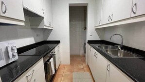 Een kleine keuken met witte kastjes, een zwart aanrecht, een ingebouwde oven en een spoelbak.
