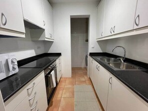Eine kleine Küche mit weißen Schränken, einer schwarzen Arbeitsplatte, einem eingebauten Backofen und einem Spülbecken.