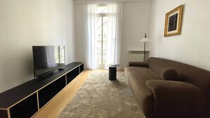Een woonkamer met een televisie, bank en een raam met gordijnen.