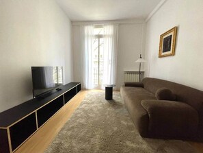 Ein Wohnzimmer mit Fernseher, Sofa und einem fensterbepflanzten Fenster.