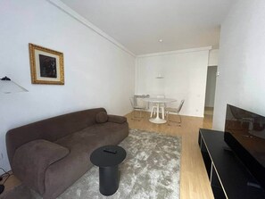 Ein modernes Wohnzimmer mit einer Couch, einem kleinen runden Tisch, einem Fernseher und einem Essbereich mit Tisch und Stühlen.