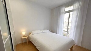 Een slaapkamer met een bed, een nachtkastje met een lamp en een raam met gordijnen.