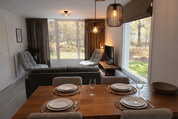 Un espace repas moderne avec une table en bois dressée pour quatre personnes, un canapé et un téléviseur posé sur une table d’appoint.