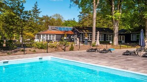 Une piscine avec des chaises longues, un bâtiment doté d’un toit en tuiles et des arbres en arrière-plan.