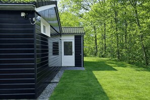 Un bâtiment moderne à l’extérieur noir, avec une porte blanche et une petite structure adjacente surmontée d’un toit en tuiles.