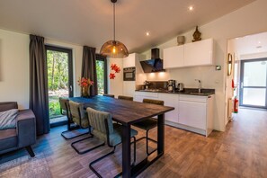 A modern kitchen with white cabinets, a dining area with a dark wooden table and chairs, and a view of greenery outside. - De Wiltzangh - Zandborg Lodge Hottub | 6p (Ruinen)
