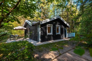 Eine Holzhütte mit Veranda, zwei Fenstern und einer kleinen Sitzecke mit Tisch und Stühlen.