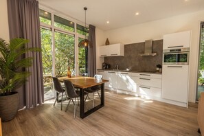 A modern kitchen with a dining area, large windows, and a potted plant. - De Wiltzangh - Heideborg Lodge Hottub | 4p (Ruinen)