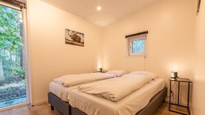 Una camera da letto con un letto, lampade da comodino, una finestra vista alberi e un quadro appeso al muro.