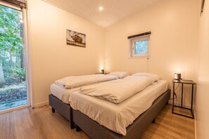 A bedroom with a bed, bedside lamps, a window with a view of trees, and a painting on the wall. - De Wiltzangh - Heideborg Lodge Hottub | 4p (Ruinen)