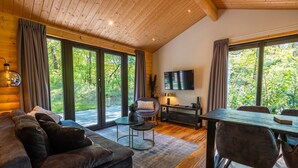 Una sala de estar moderna con sofá, televisión y comedor, ventanas amplias y techo de madera.