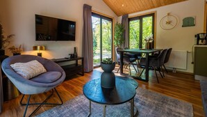 Una sala moderna con un televisor de pantalla plana, un sillón cómodo, una zona de comedor con mesa y sillas, y un ventanal con cortinas.