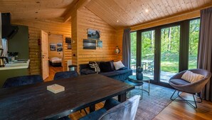 Interior acogedor de una cabaña con comedor, sofá y vistas al exterior.