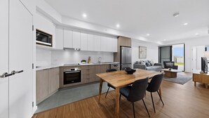 Uma cozinha moderna com armários brancos, uma mesa de jantar de madeira e um sofá cinza na sala de estar.