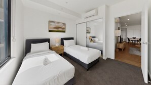 Quarto de hotel moderno com duas camas, um espelho grande, um quadro e vista para a área de refeições.