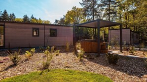 Una cabaña moderna con un espacio al aire libre cubierto, rodeada de un paisaje boscoso.