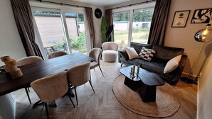 Una sala de estar moderna con una mesa de comedor, sofá y mesa de centro, ventanas amplias y vistas al exterior.